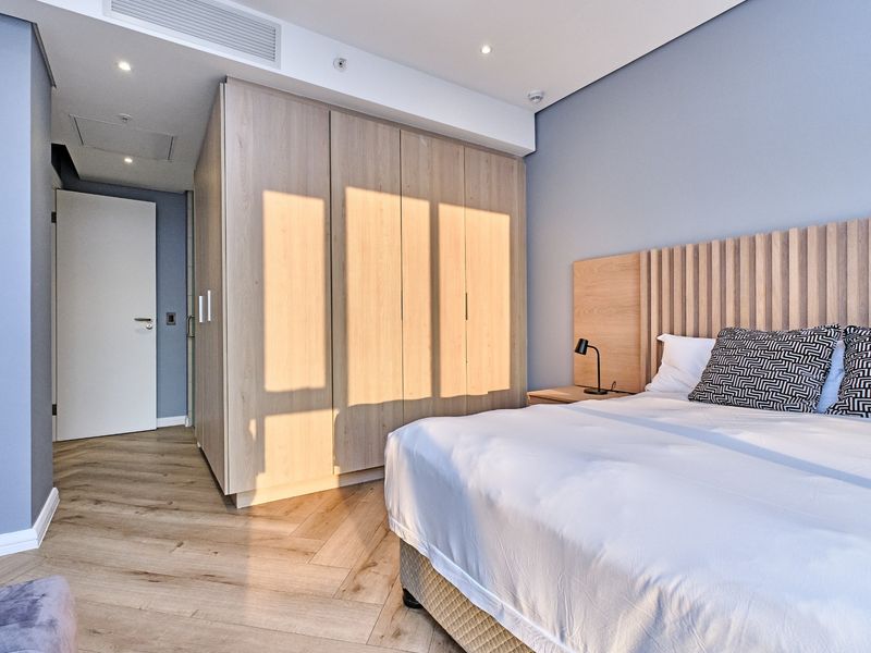 Modern bedroom featuring herringbone timber flooring, a large built-in wardrobe, and a custom timber headboard with integrated lighting.