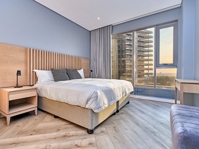 Modern bedroom featuring herringbone timber flooring, a custom timber slat headboard feature wall, and floor-to-ceiling windows with expansive city views.
