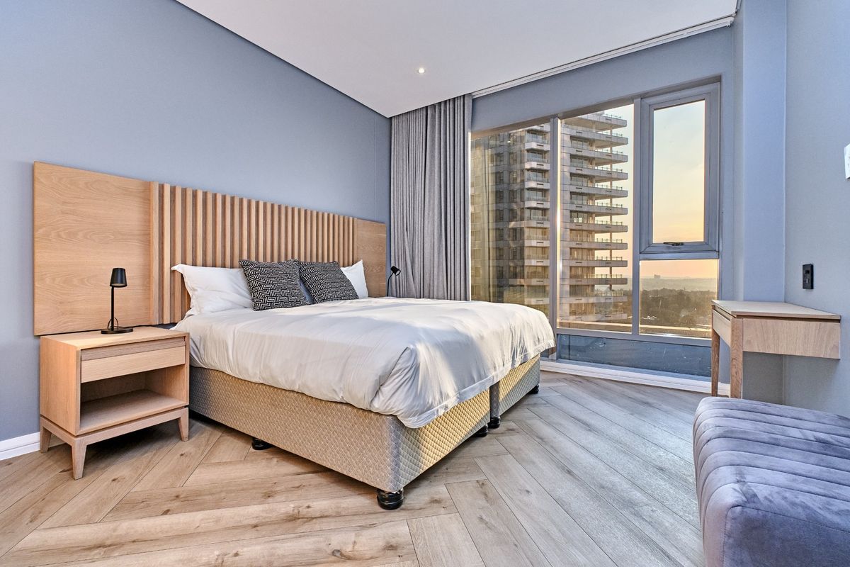 Modern bedroom featuring herringbone timber flooring, a custom timber slat headboard feature wall, and floor-to-ceiling windows with expansive city views.