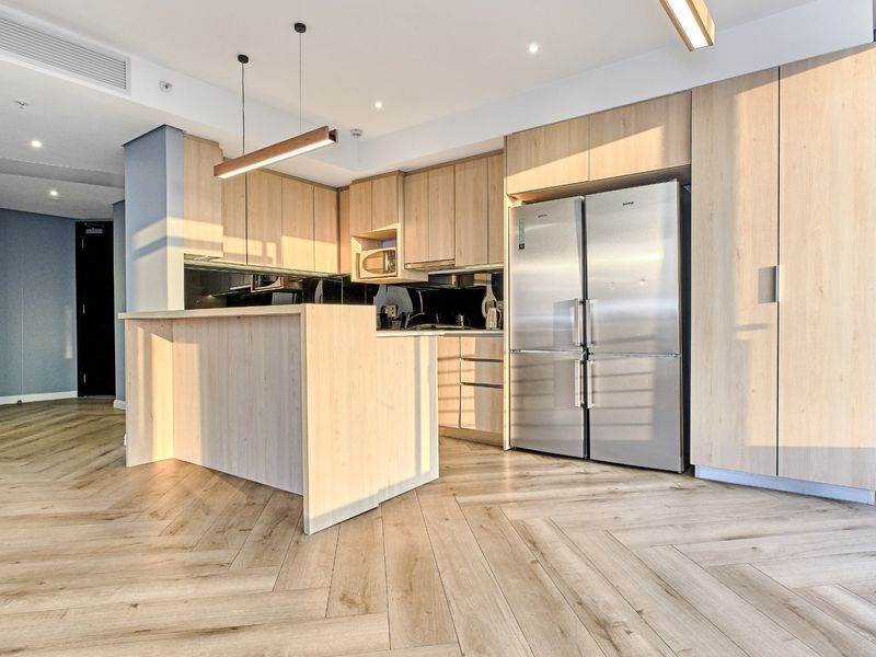 Modern kitchen featuring light wood cabinetry, a functional island, herringbone flooring, and integrated stainless steel appliances in a bright, contemporary open-plan setting.