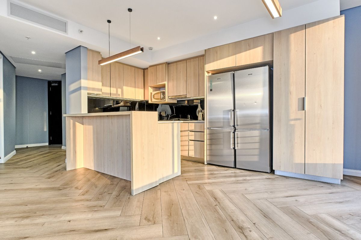 Modern kitchen featuring light wood cabinetry, a functional island, herringbone flooring, and integrated stainless steel appliances in a bright, contemporary open-plan setting.