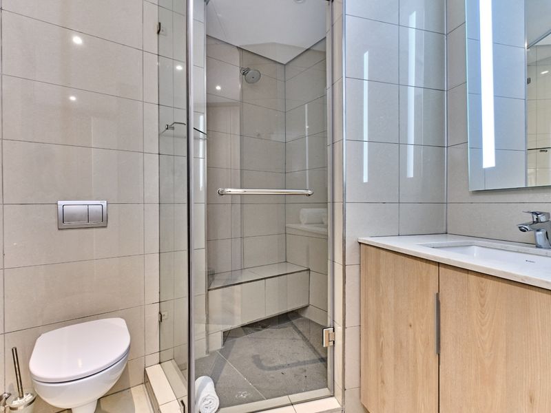 Modern bathroom featuring a glass-enclosed shower with a built-in bench, wall-mounted toilet, and a sleek vanity with an integrated basin.
