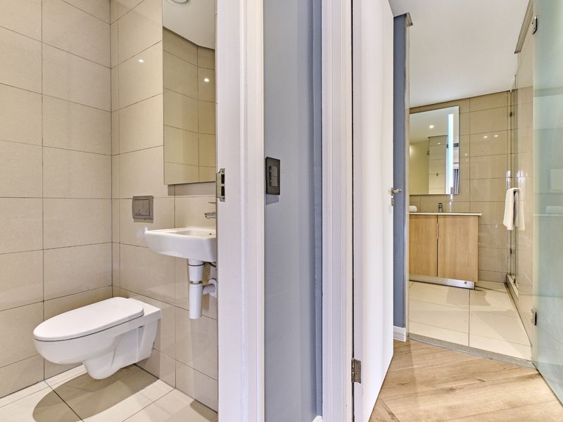 Modern bathroom featuring a wall-mounted toilet, sleek basin, vanity cabinet, and a glass-enclosed shower with neutral tiled finishes.