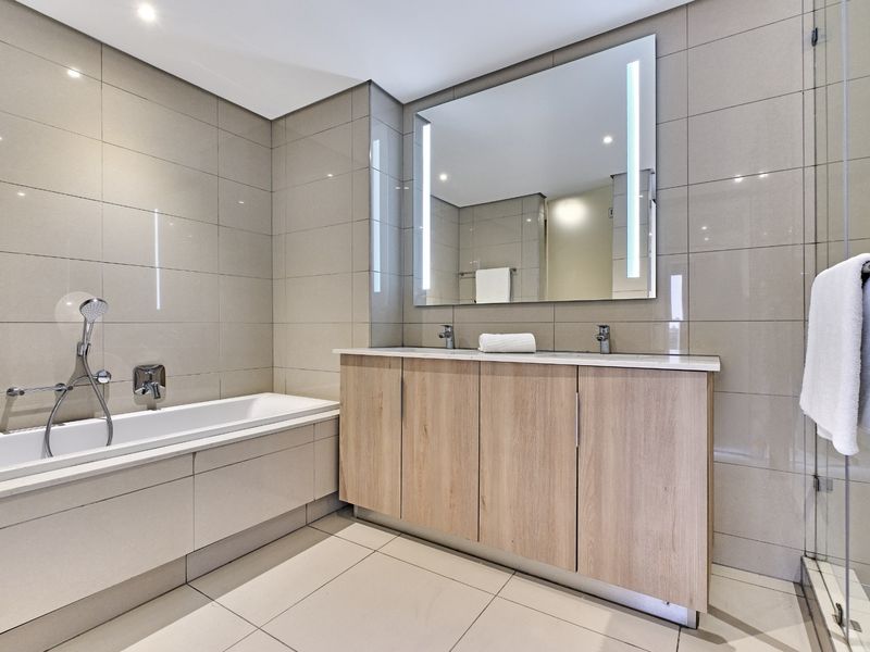 Modern bathroom featuring a double vanity with wood-finish cabinetry, a built-in bathtub, and a glass-enclosed shower with neutral floor-to-ceiling tiling.