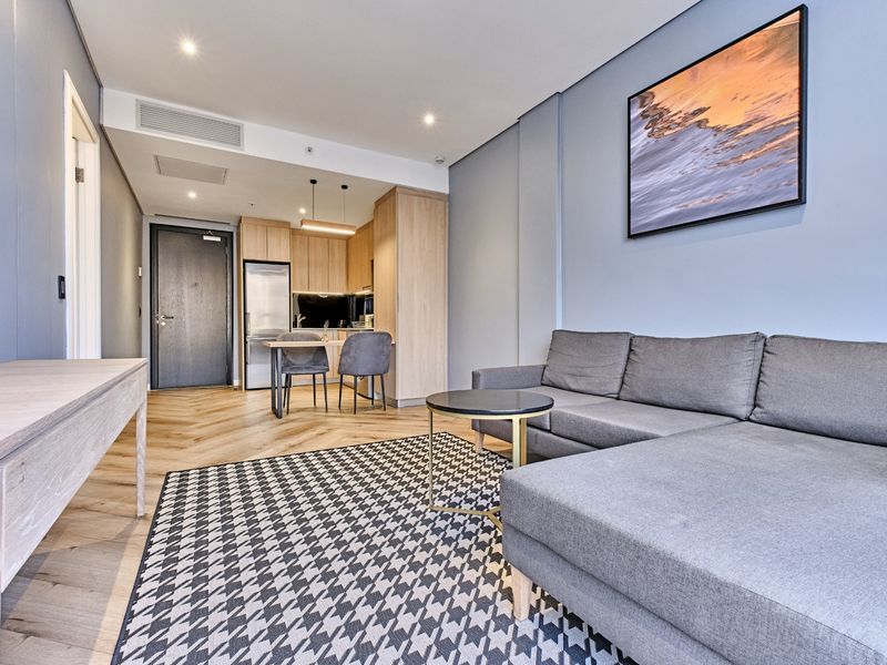 Modern open-plan living area featuring herringbone timber flooring, recessed lighting, and a sleek, integrated kitchen with contemporary cabinetry.