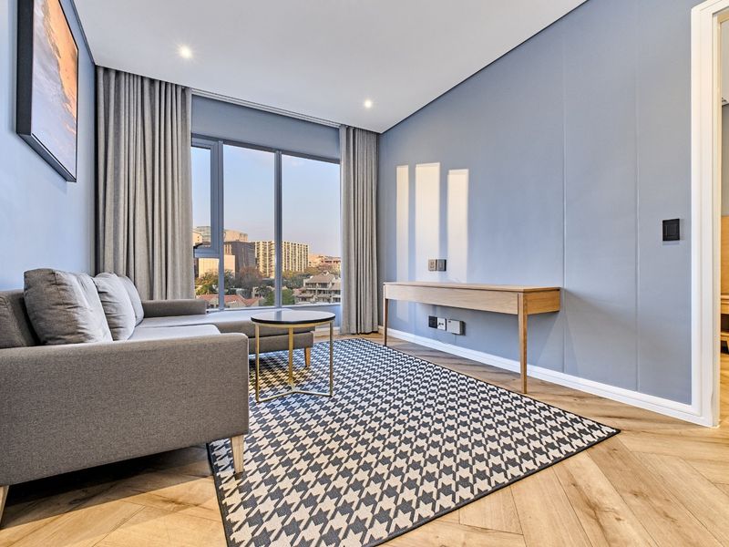Modern living room featuring herringbone timber flooring, floor-to-ceiling windows with city views, and recessed downlighting in a contemporary apartment setting.