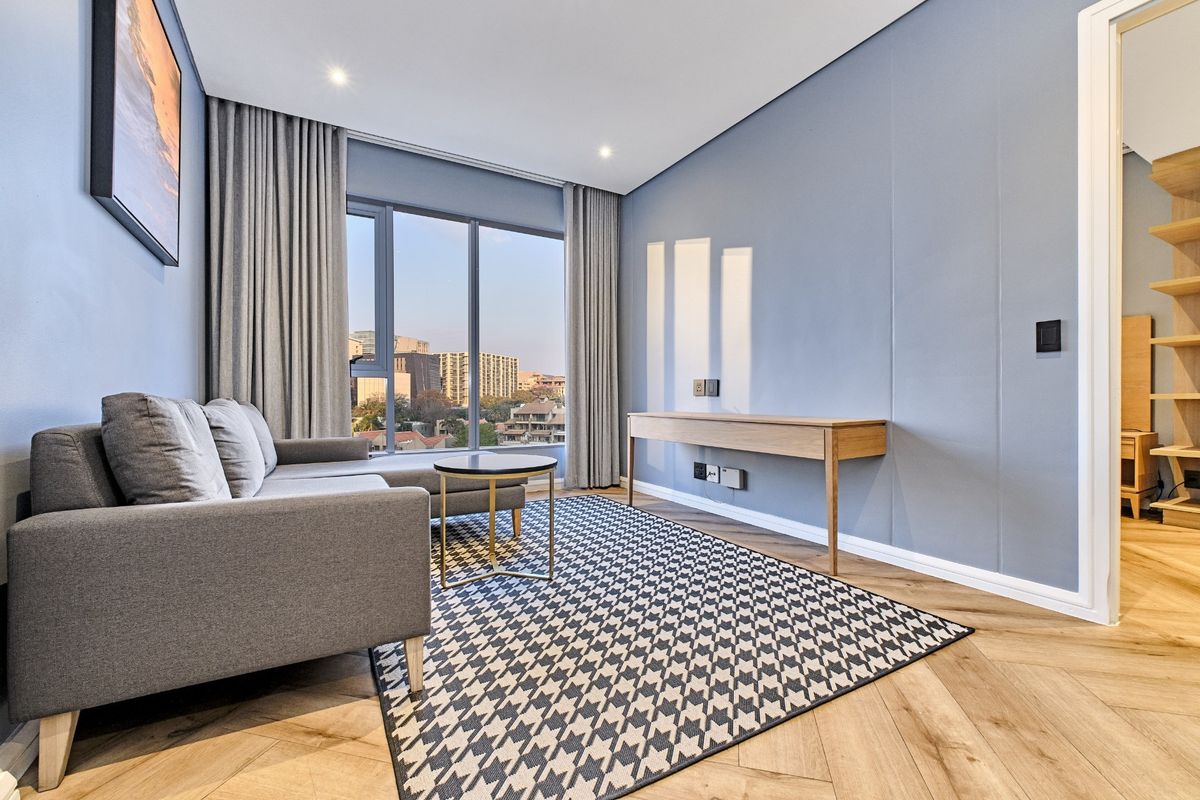 Modern living room featuring herringbone timber flooring, floor-to-ceiling windows with city views, and recessed downlighting in a contemporary apartment setting.