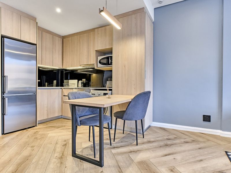 Modern open-plan kitchen featuring light oak cabinetry, herringbone wood flooring, and integrated appliances, creating a sleek and functional living space.