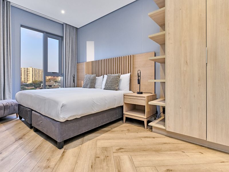 Modern bedroom featuring herringbone timber flooring, a custom slatted timber headboard, built-in cabinetry, and large windows with views.