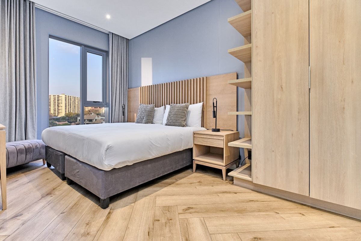 Modern bedroom featuring herringbone timber flooring, a custom slatted timber headboard, built-in cabinetry, and large windows with views.