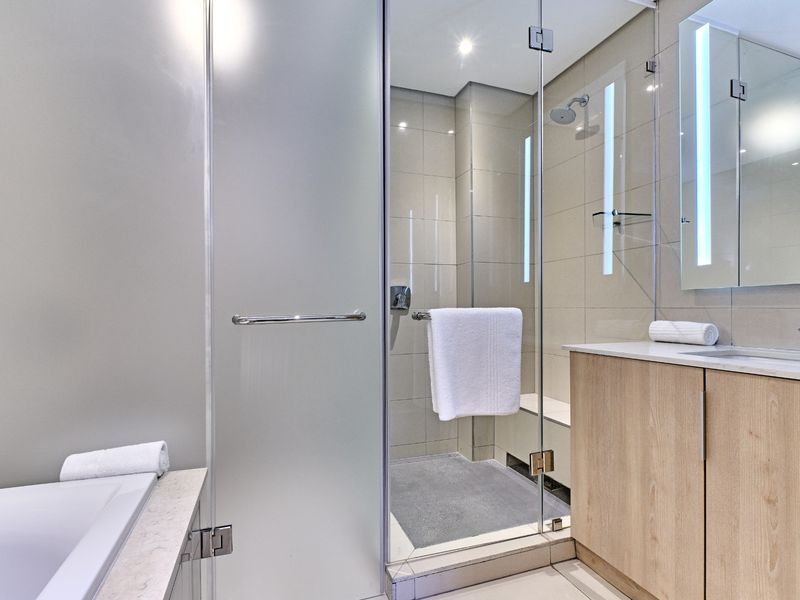 Modern bathroom featuring a glass-enclosed shower, built-in vanity with integrated sink, and a bathtub with clean, contemporary tiling.