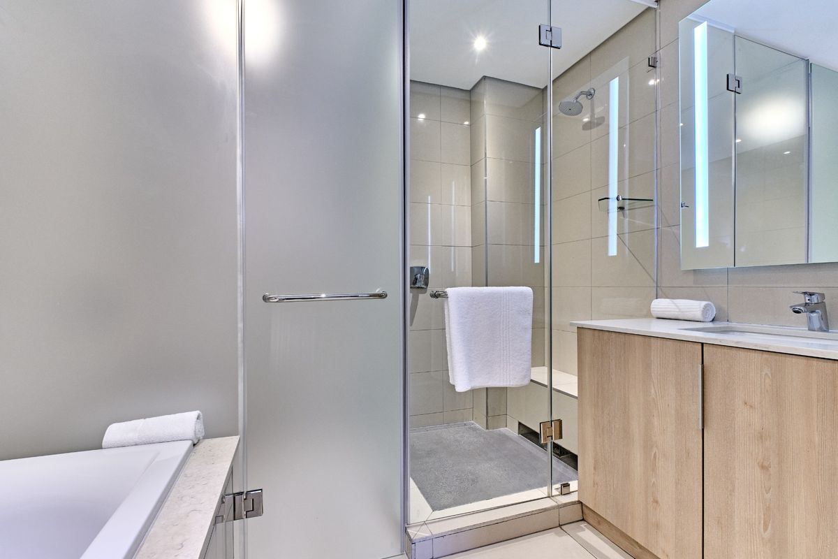 Modern bathroom featuring a glass-enclosed shower, built-in vanity with integrated sink, and a bathtub with clean, contemporary tiling.