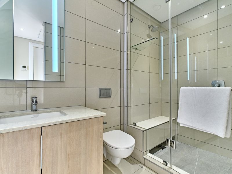 Modern bathroom featuring a vanity with stone countertop, wall-hung toilet, and a spacious glass-enclosed shower with a built-in bench and neutral tiling.