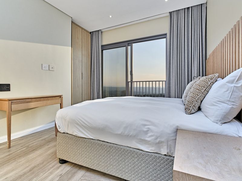 Modern bedroom featuring laminate flooring, built-in wardrobe, timber slat headboard, and a sliding glass door opening to a balcony with scenic views.