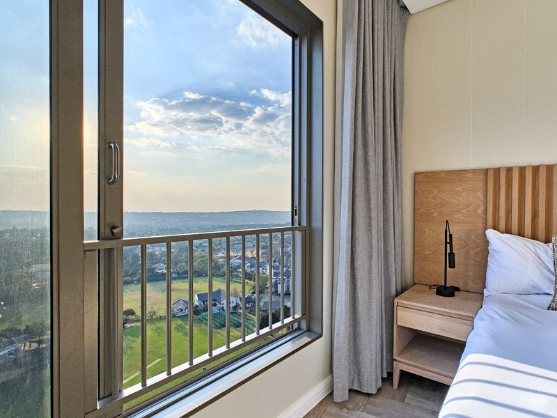 A modern bedroom featuring a large sliding glass door with a safety railing, offering expansive elevated views of the surrounding landscape.