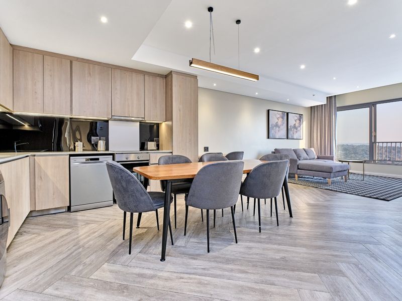 Modern open-plan living area featuring a contemporary kitchen with light wood cabinetry, herringbone flooring, and seamless access to a private balcony.