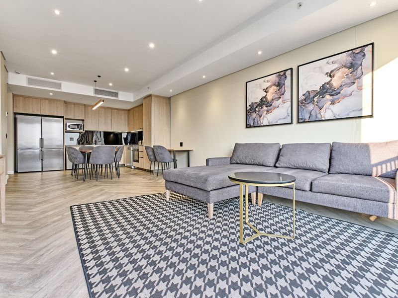 Modern open-plan living area featuring herringbone flooring, recessed lighting, and a sleek, well-appointed kitchen with integrated cabinetry.