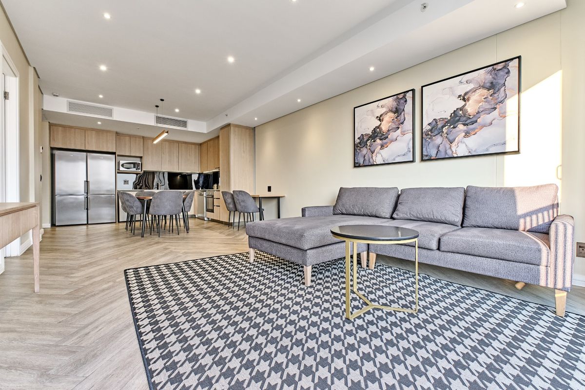 Modern open-plan living area featuring herringbone flooring, recessed lighting, and a sleek, well-appointed kitchen with integrated cabinetry.