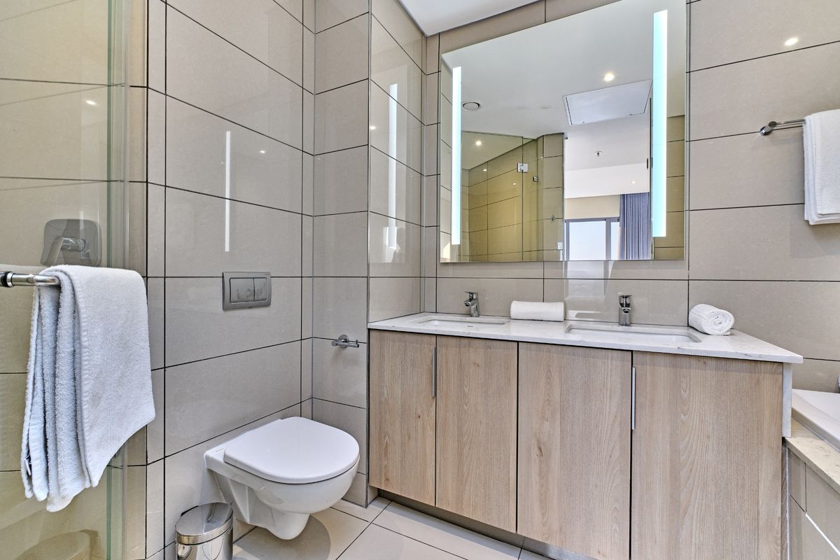 Modern bathroom featuring a double vanity with stone countertop, wall-mounted toilet, glass shower enclosure, and elegant floor-to-ceiling tiling.