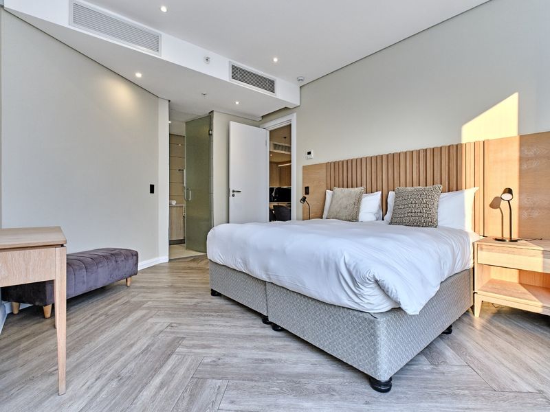 Modern bedroom featuring herringbone flooring, integrated ducted air conditioning, and a custom timber headboard with an en-suite bathroom access.