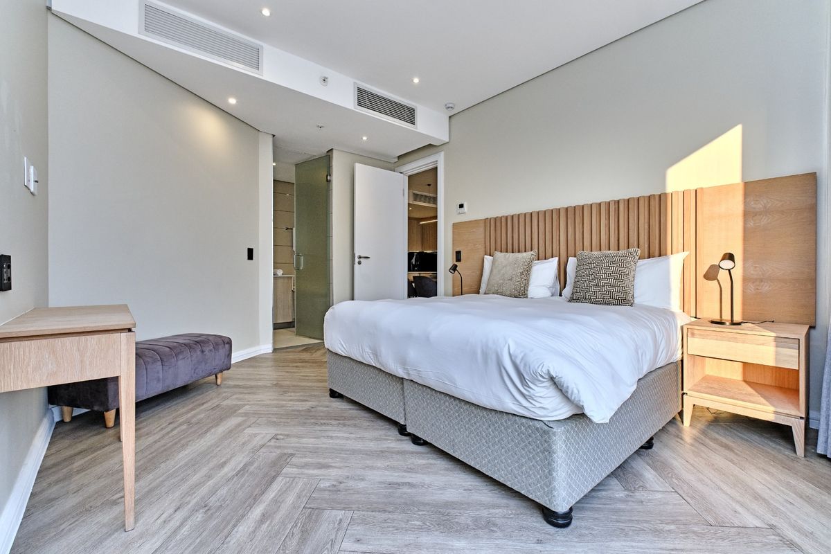 Modern bedroom featuring herringbone flooring, integrated ducted air conditioning, and a custom timber headboard with an en-suite bathroom access.