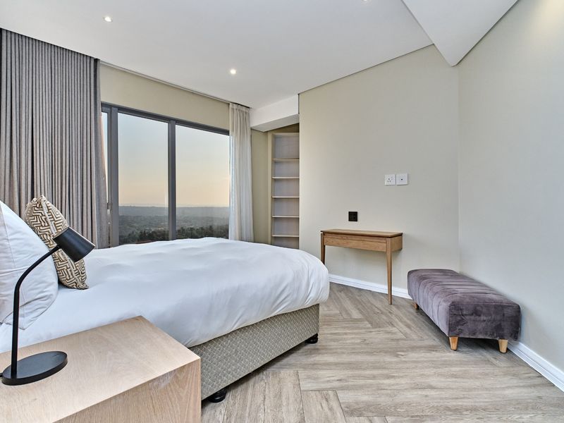 Modern bedroom featuring herringbone flooring, built-in shelving, and expansive floor-to-ceiling windows offering scenic views.