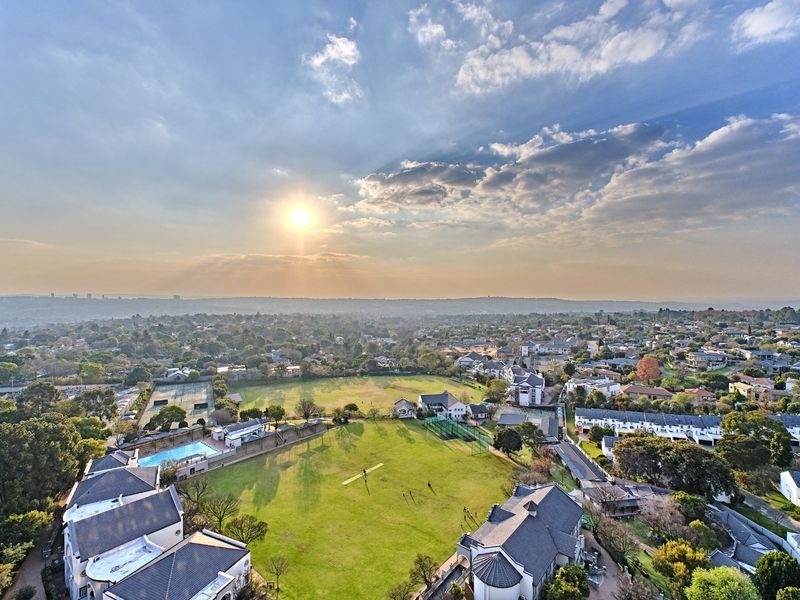 An elevated aerial view of the residential estate, showcasing the surrounding neighborhood, communal green spaces, swimming pool, and tennis court facilities.