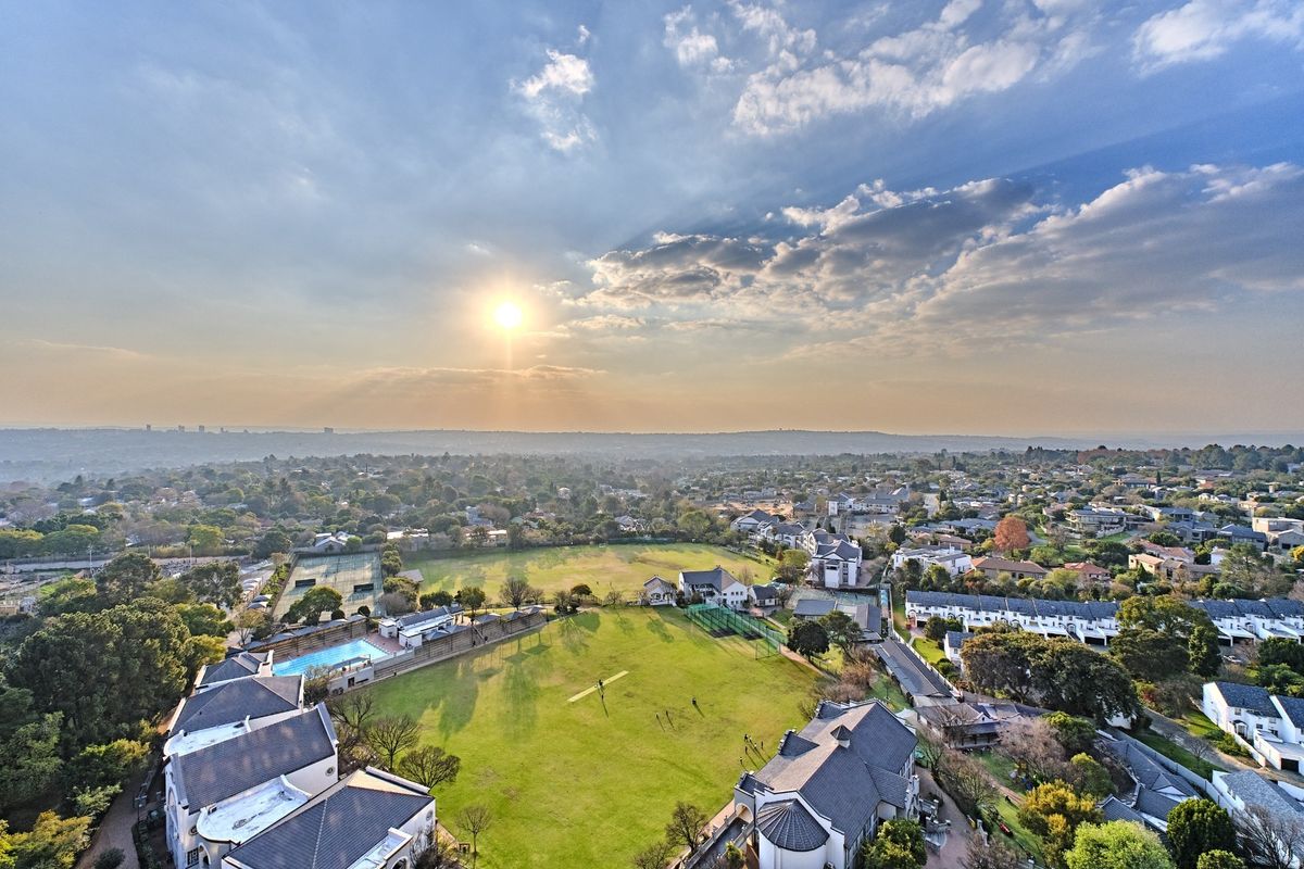 An elevated aerial view of the residential estate, showcasing the surrounding neighborhood, communal green spaces, swimming pool, and tennis court facilities.