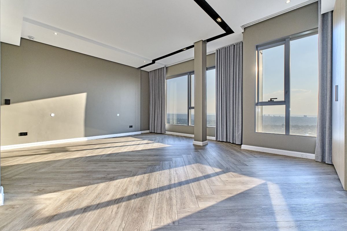 A bright, modern living area featuring high-quality herringbone wood flooring, expansive windows with panoramic views, and sleek recessed ceiling details.
