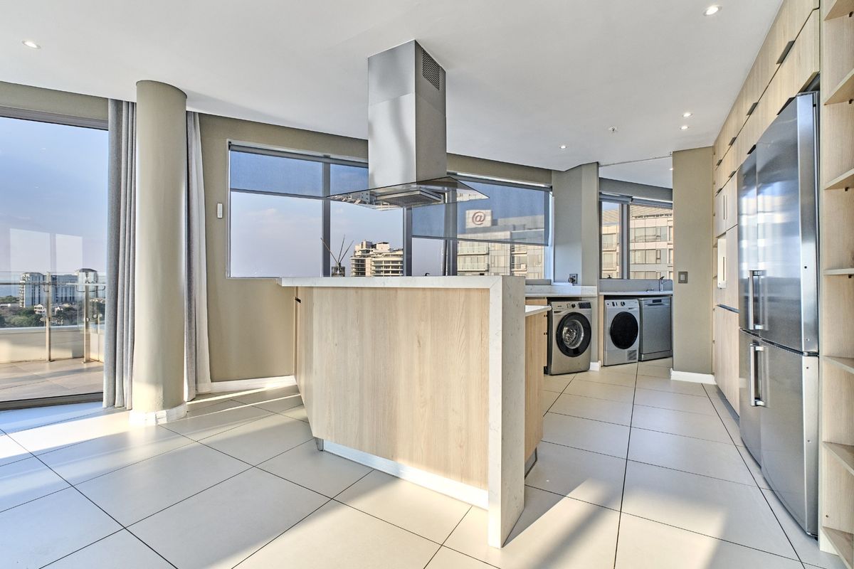 Modern open-plan kitchen featuring light wood cabinetry, stone countertops, a central island with an extractor fan, and large windows with city views.