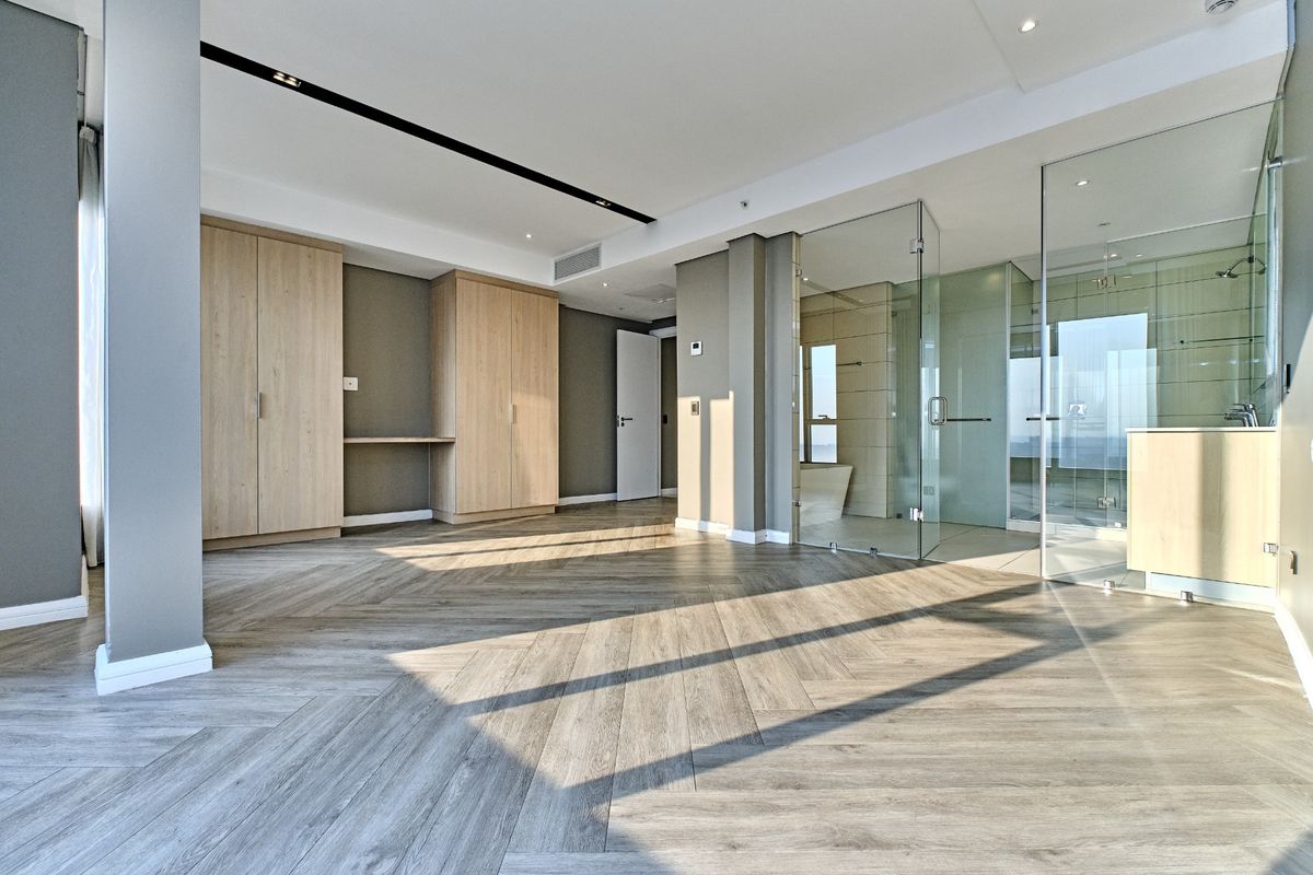 Spacious modern bedroom featuring herringbone wood flooring, built-in cabinetry, and a sleek glass-enclosed en-suite bathroom with contemporary finishes.