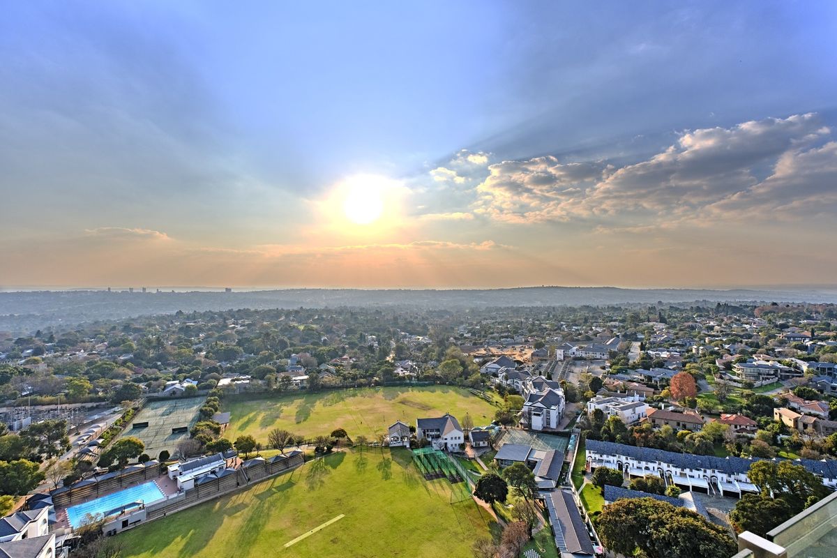 An elevated aerial view showcasing the surrounding residential neighborhood, including communal swimming pool and tennis court facilities.