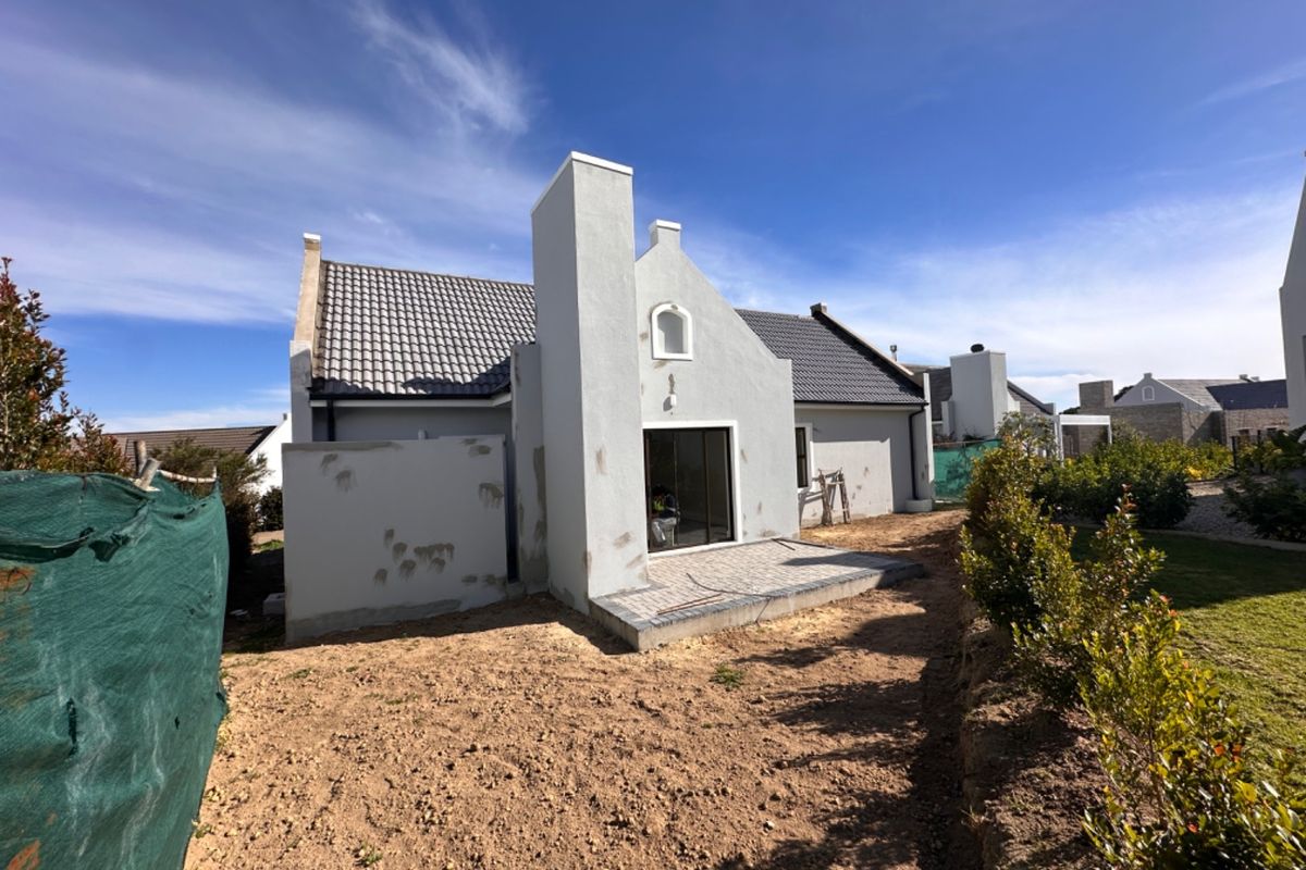 Rear view of the property featuring a tiled roof, chimney, and a paved patio area with unfinished exterior wall plastering.