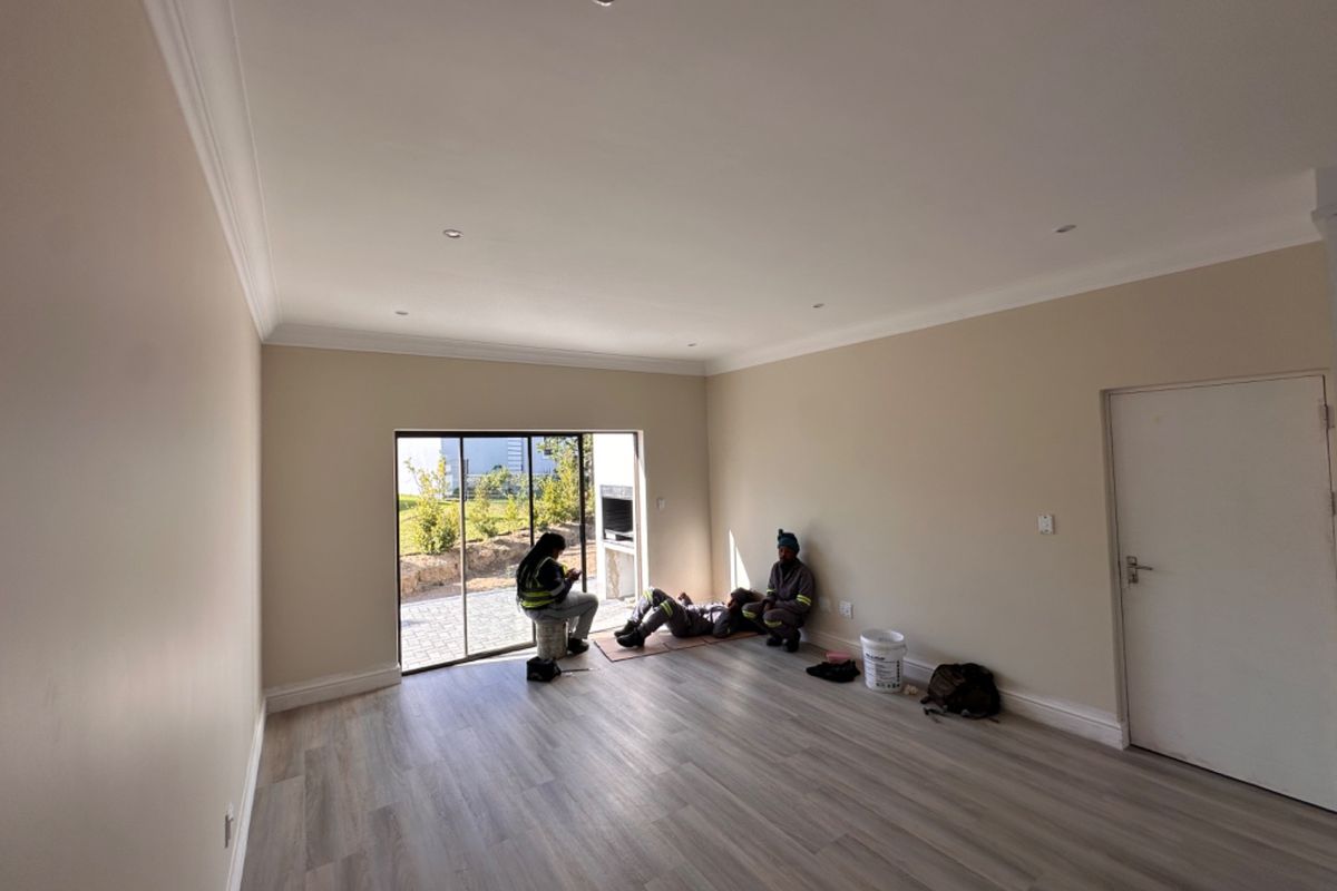 A bright, empty living room featuring modern laminate flooring, recessed downlights, and a large sliding glass door leading to an outdoor area.