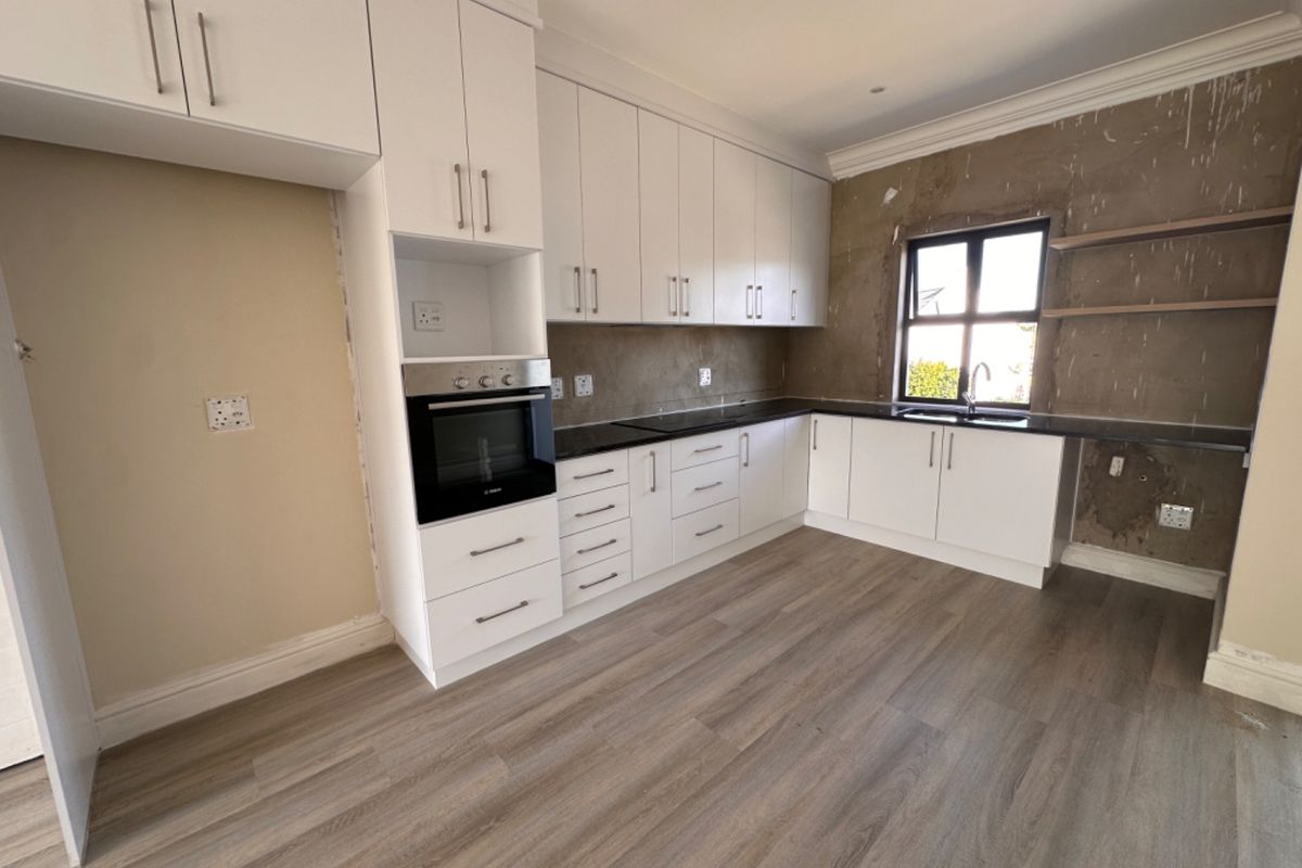 A partially completed kitchen featuring white cabinetry, built-in oven, and dark countertops, requiring final wall finishes and backsplash installation.