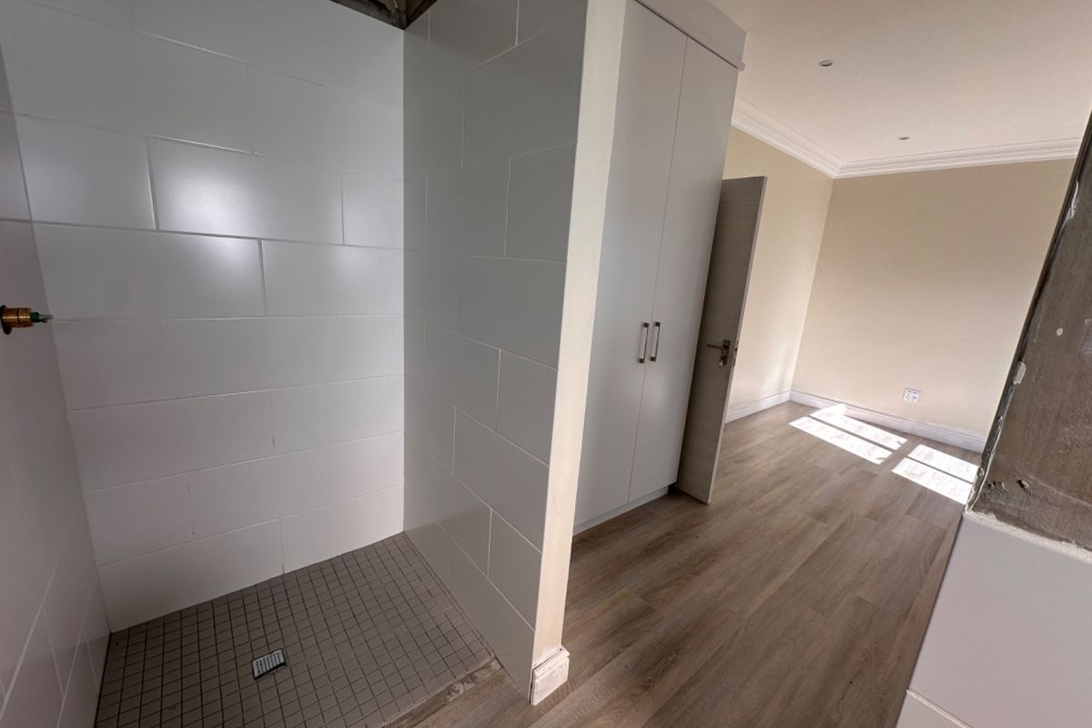 A bedroom featuring an integrated shower enclosure, built-in wardrobe, and laminate flooring, currently undergoing finishing touches and renovation work.