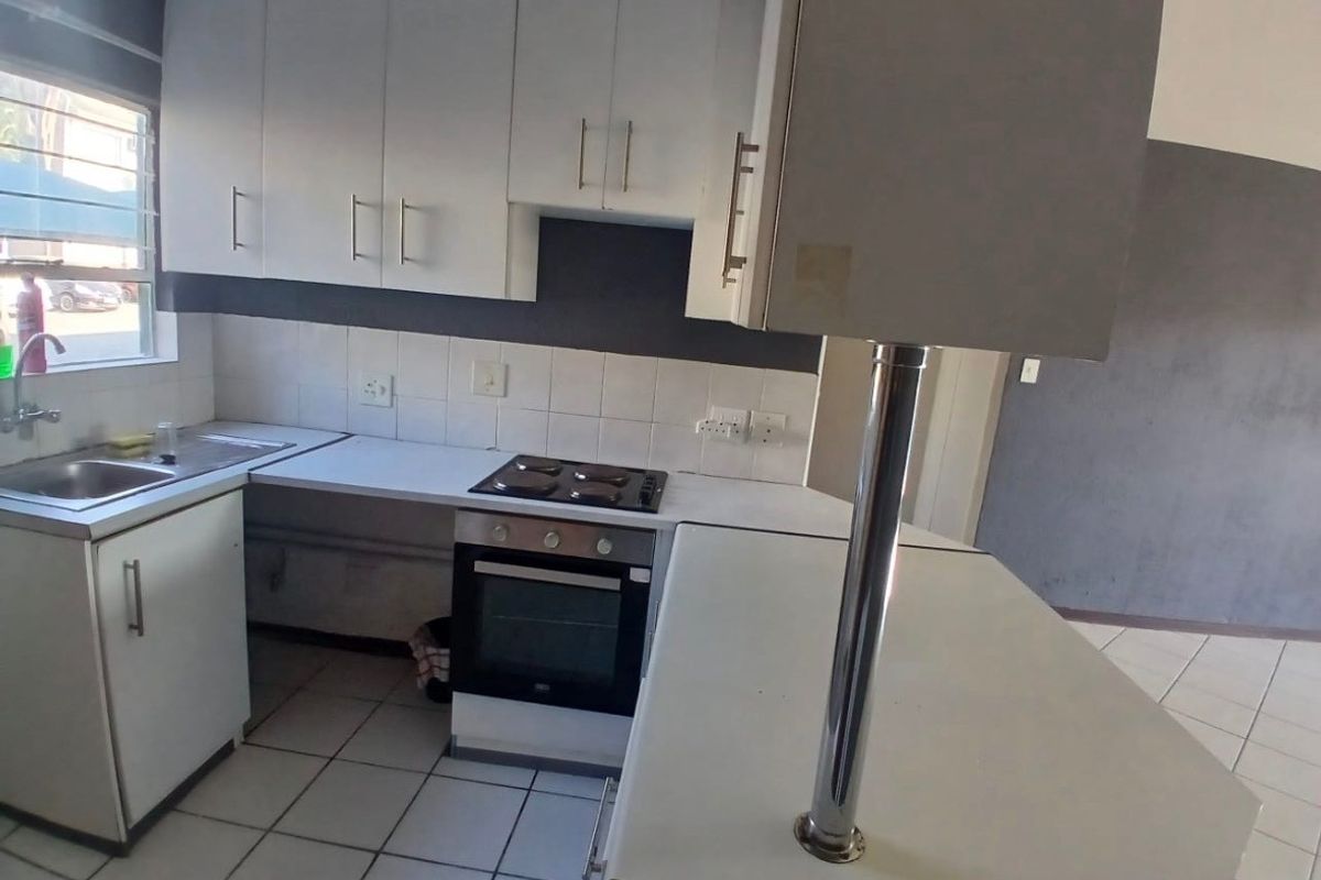 A functional kitchen featuring white cabinetry, a built-in oven and hob, tiled backsplash, and a breakfast bar, offering a clean and practical workspace.