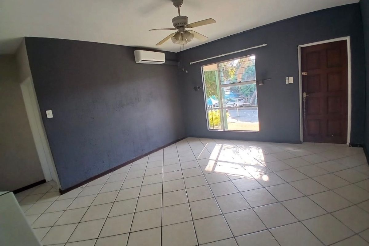An empty living room featuring tiled flooring, a ceiling fan, and a wall-mounted air conditioning unit with dark-painted walls.