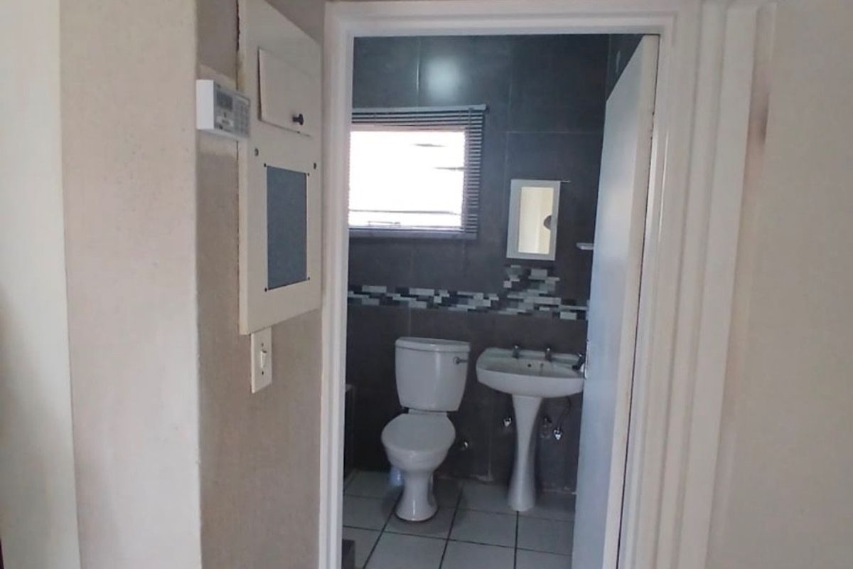 A compact bathroom featuring a pedestal basin, toilet, and tiled finishes, viewed from an adjacent hallway.
