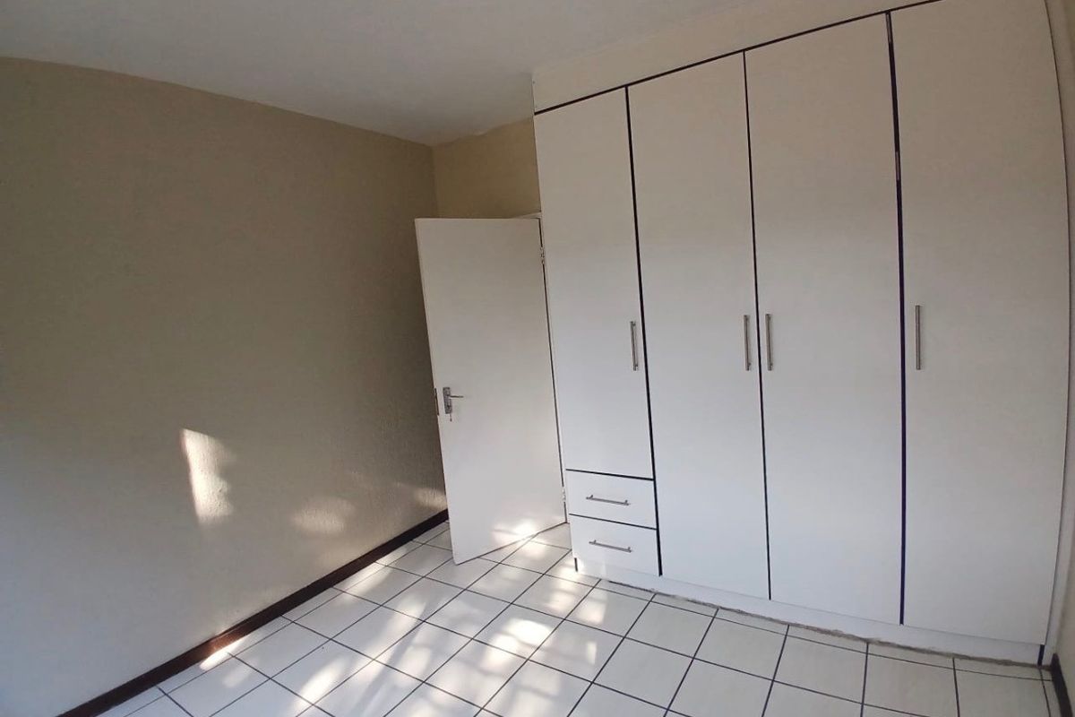 A clean, empty bedroom featuring white built-in cupboards and neutral tiled flooring, offering a blank canvas for personalization.