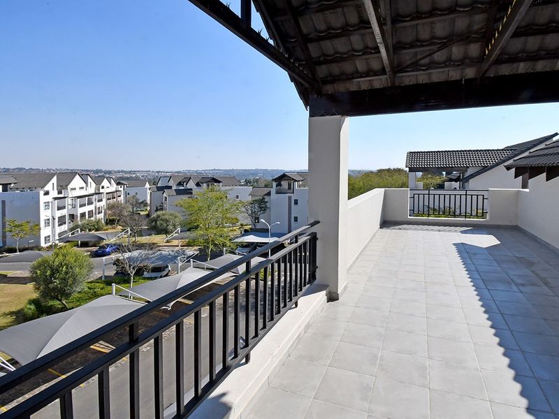 A spacious covered balcony featuring tiled flooring and metal railings, offering an elevated view of the surrounding apartment complex and parking area.