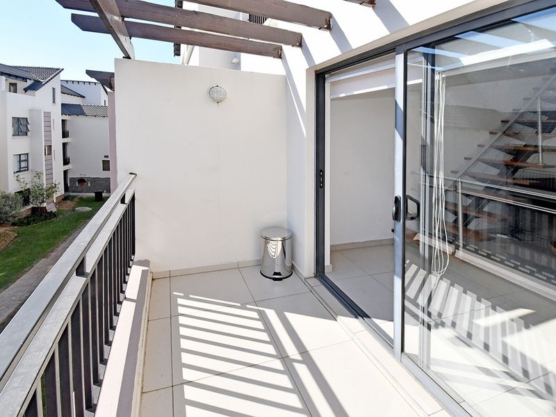 A clean, tiled balcony featuring a wooden pergola, metal balustrade, and sliding glass door access to the interior living space.