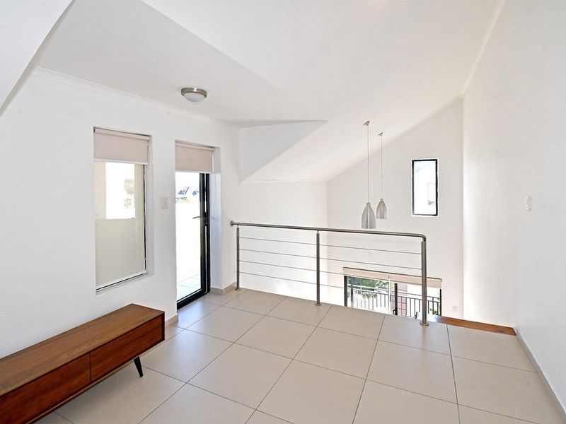 A bright, open-plan landing area featuring tiled flooring, a modern stainless steel balustrade, and high sloped ceilings with pendant lighting.