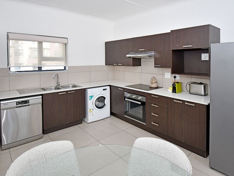 Modern kitchen featuring dark wood cabinetry, stone countertops, integrated appliances, and tiled flooring, offering a clean and functional workspace.