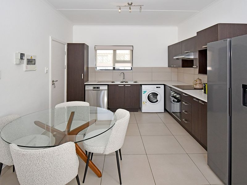 Modern open-plan kitchen featuring dark wood cabinetry, integrated appliances, tiled flooring, and a functional layout with ample counter space.