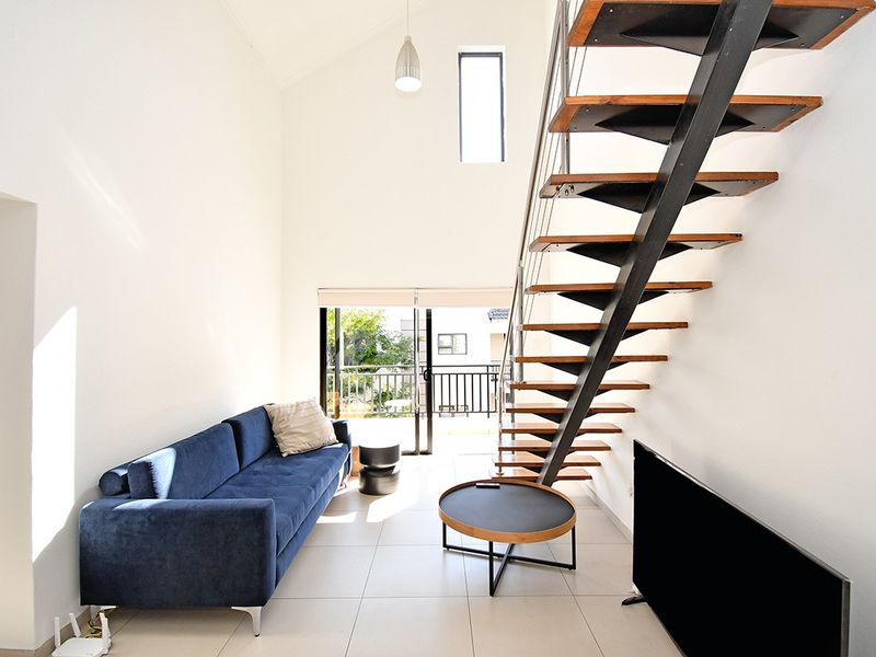 Bright living room featuring a modern open-tread staircase, high vaulted ceilings, tiled flooring, and direct access to a private balcony through sliding glass doors.