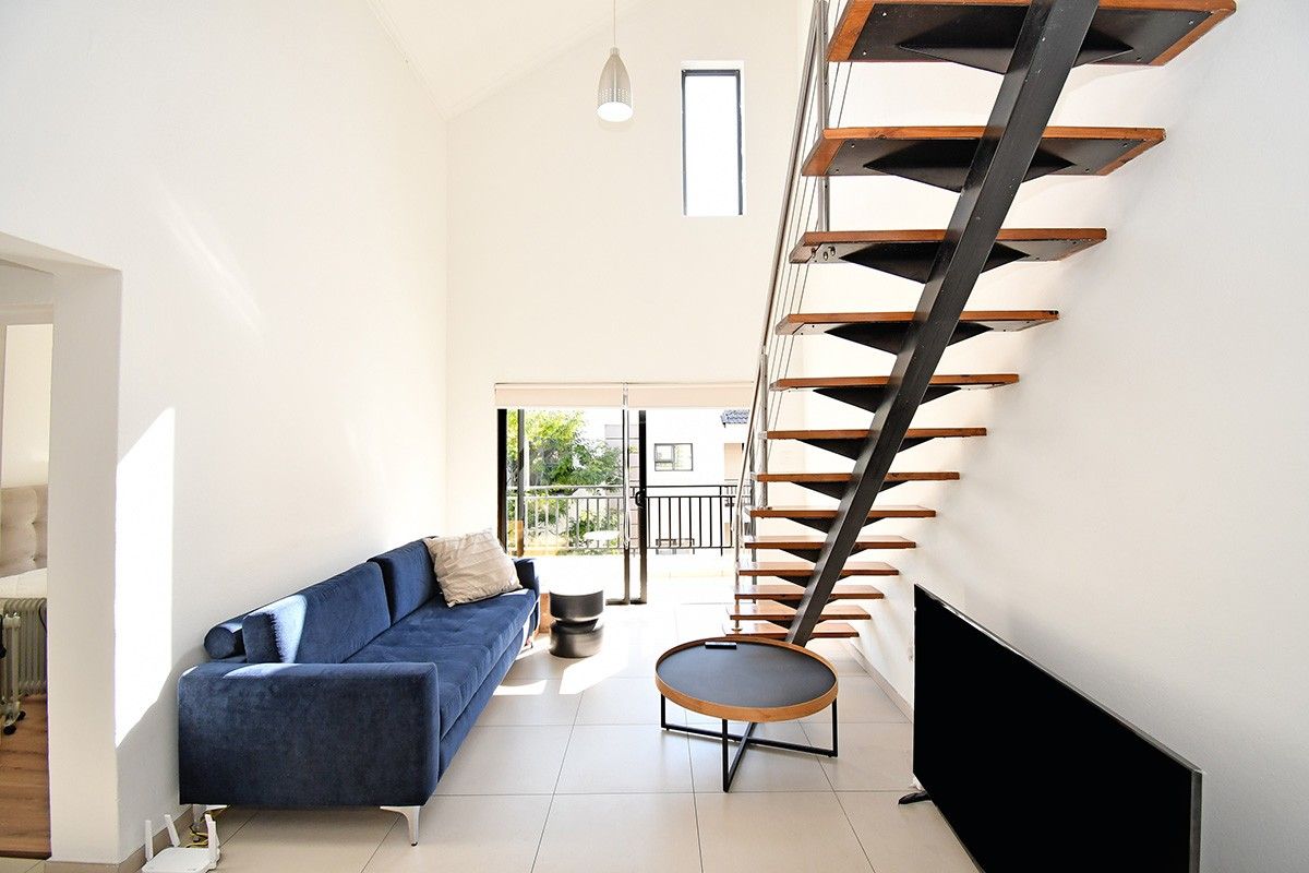Bright living room featuring a modern open-tread staircase, high vaulted ceilings, tiled flooring, and direct access to a private balcony through sliding glass doors.