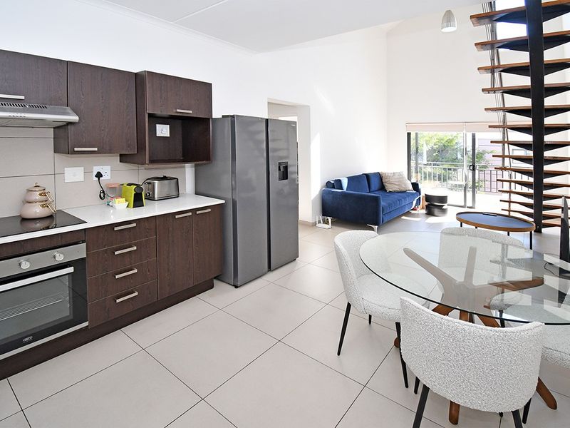 Modern open-plan kitchen and living area featuring dark wood cabinetry, tiled floors, and a striking spiral staircase leading to the upper level.