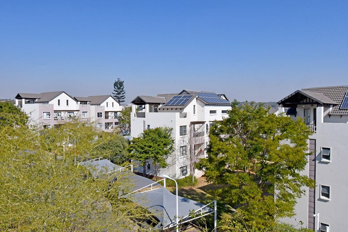 An elevated view of a modern apartment complex featuring tiled roofs, installed solar panels, and shaded parking structures within a landscaped residential setting.