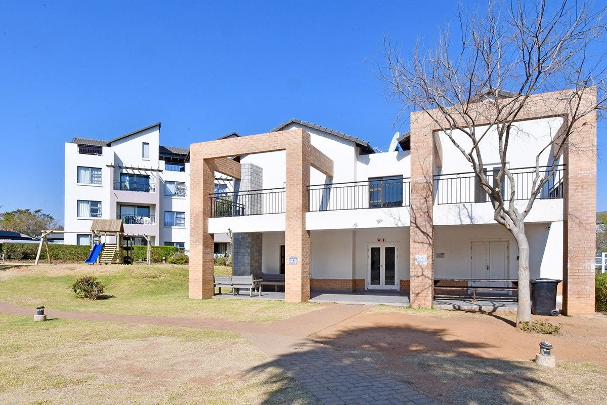 Rear view of the apartment complex featuring a brick facade, covered patio area, and upper-level balcony with metal railings.